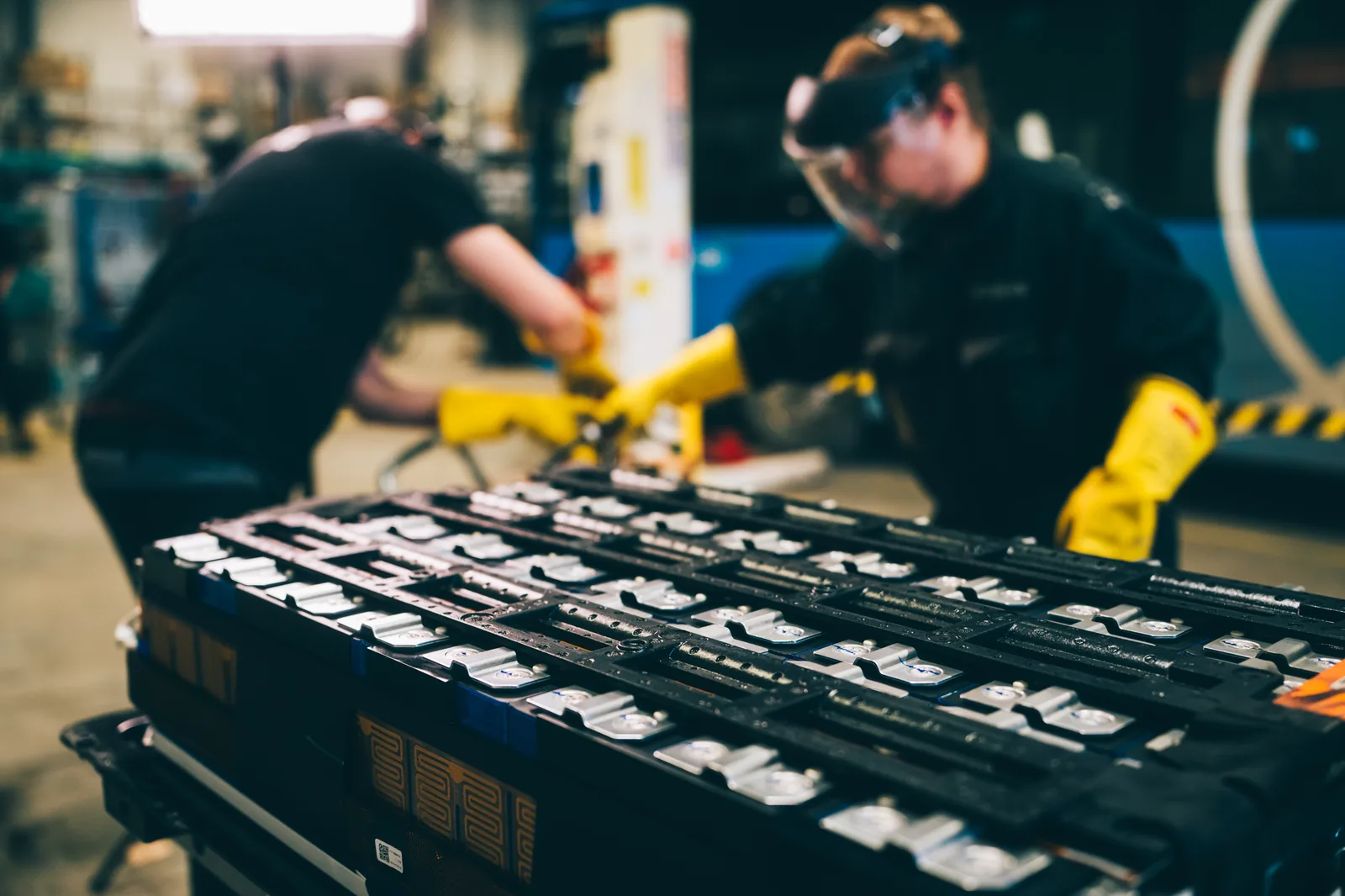 YES-EU high-voltage specialists in face shields and insulated gloves working on a traction battery module in the workshop
