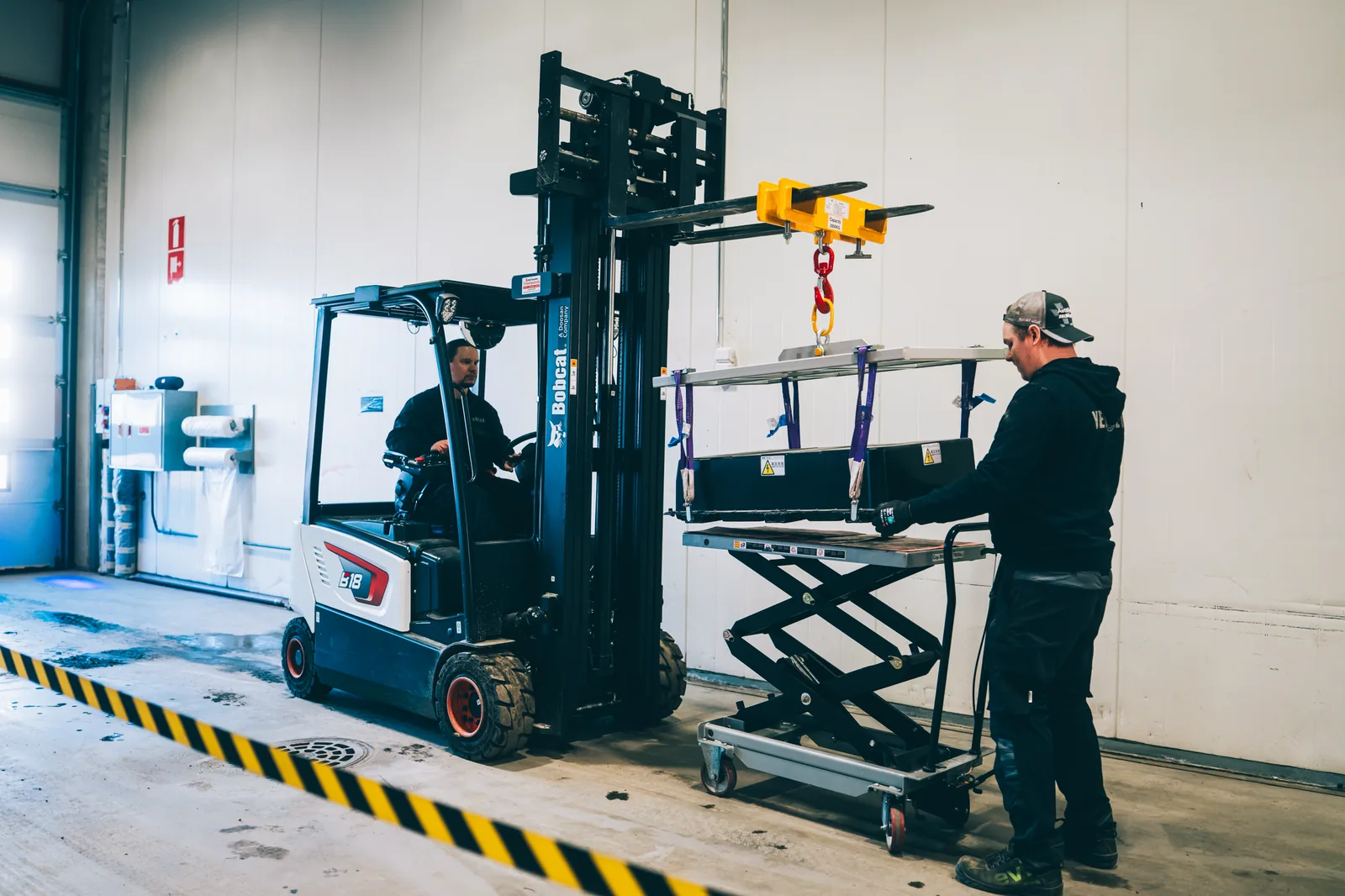 Two YES-EU colleagues moving a battery module between a forklift and a lifting table in the workshop